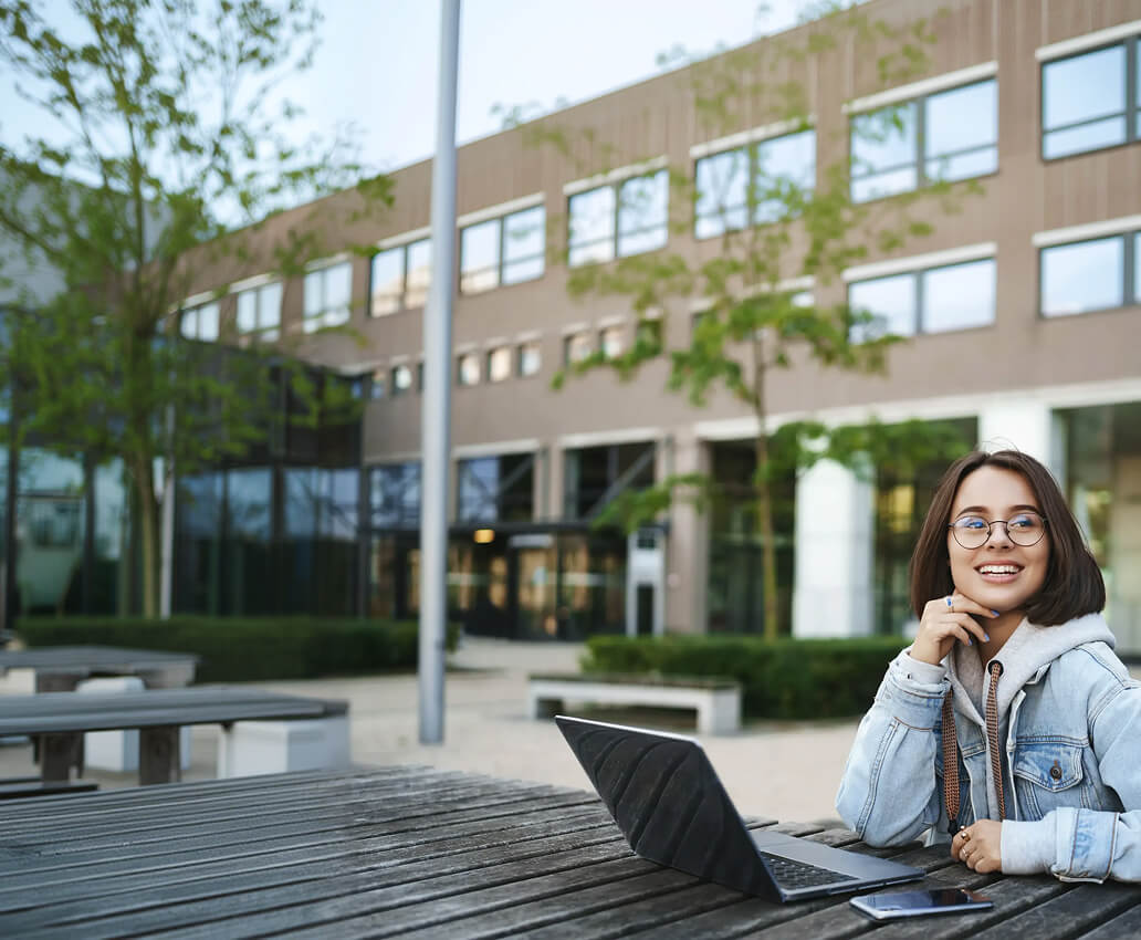 Estudiante con portátil sentada en una mesa exterior del campus